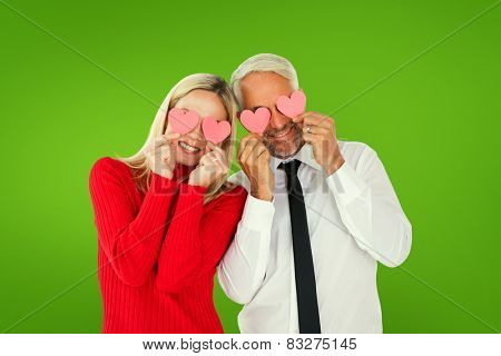 Silly couple holding hearts over their eyes against green vignette
