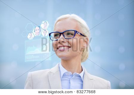 business, people, future technology and communication concept - young smiling businesswoman in eyeglasses with virtual screen, video chat and charts projection outdoors