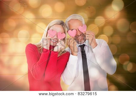 Silly couple holding hearts over their eyes against light circles on black background