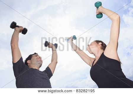 A Young, caucasian couple working out with dumbbells outside