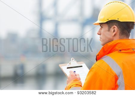 Rear view of mid adult man writing on clipboard in shipping yard