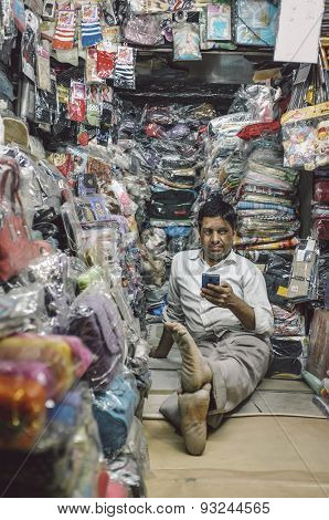 JODHPUR, INDIA - 07 FEBRUARY 2015: Store owner sits on floor of little textile shop overflown with different merchandise and waits for customers. Post-processed with added grain and texture.