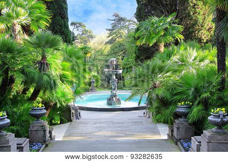 Walkway In A Beautiful Park With Palms, Thuyas And Fountain