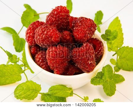 raspberries in a white plate with mint on a white table
