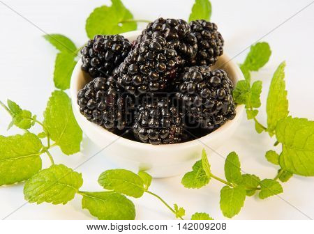 blackberries in a white plate with mint on a white table