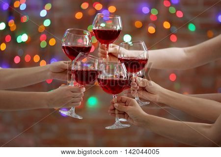 Female hands clinking glases with red wine on bokeh background