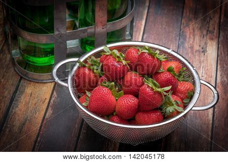 Fresh strawberries in stainless steel colander on a wood surface
