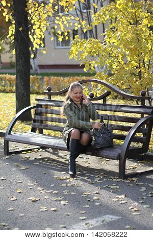 girl talking on the phone outdoors on a bench on a sunny autumn day