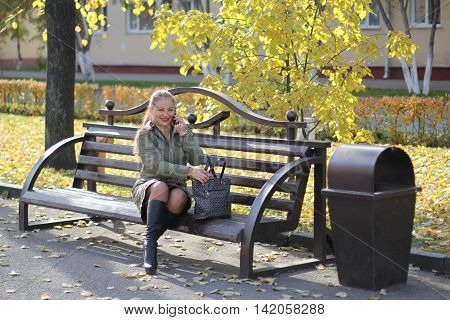 girl talking on the phone outdoors on a bench on a sunny autumn day