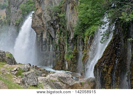 Kapuzbashi waterfalls down to river. Lush vegetation on rock surface. Turkey Aladaglar mountains.