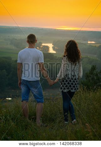 romantic couple looking into the distance at sunset on outdoor, beautiful landscape and bright yellow sky, love tenderness concept, young adult people