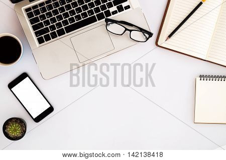 White office desk table with laptop pencil eyeglasses blank screen smartphone blank leather notebook and cup of coffee. Top view with copy space