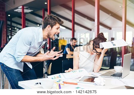 Mad crazy young businessman arguing with sad stressed businesswoman at work in office