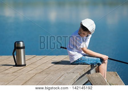 Boy fishing on the pier and looking for tea in a thermos