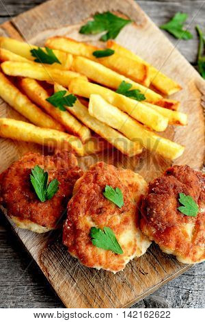 Turkey breast cutlets served with deep fried potatoes on cutting board and on an old wooden background. Cutlets prepared from minced meat and fried in vegetable oil in a frying pan. Closeup. Top view