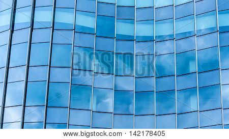 Perspective and underside angle view to textured background of contemporary glass facade of achitecture building skyscrapers with the light reflect of sky and cloud. (Detail curve shape of glass with vertical and horizontal mullion)
