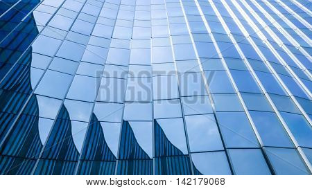 Perspective and underside angle view to textured background of contemporary glass facade of achitecture building skyscrapers with the light reflect of sky and cloud. (Detail curve shape of glass with vertical and horizontal mullion)
