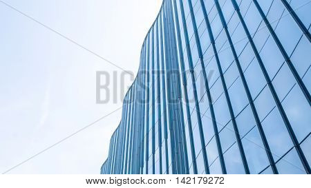 Perspective and underside angle view to textured background of contemporary glass facade of achitecture building skyscrapers with the light reflect of sky and cloud. (Detail curve shape of glass with vertical and horizontal mullion)