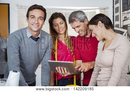 Confident Tailor Standing With Team Using Tablet Computer