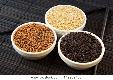 black red and white unpolished rice in white plates on a black straw mat