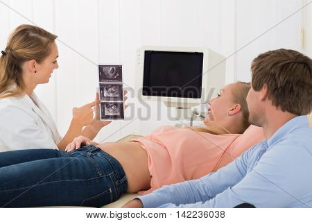 Female Doctor Showing Ultrasound Scan To Pregnant Woman And Her Husband