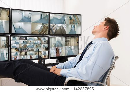 Security Guard Sleeping In Front Of Multiple Computers Showing CCTV Footage