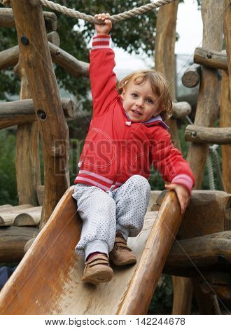 Little girl in red sweatshirt playing on wooden slipway