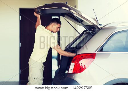 road trip, transport, private property leisure and people concept - young man with open car trunk at parking space