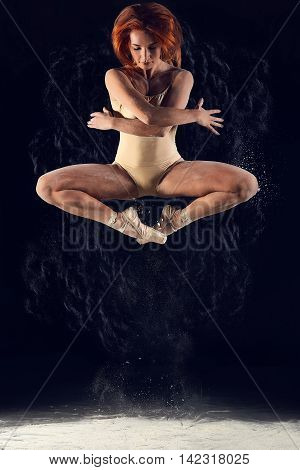 Dancer high jump and the explosion of white dust. Dramatic portrait of strong woman dancer with white powder on black background.