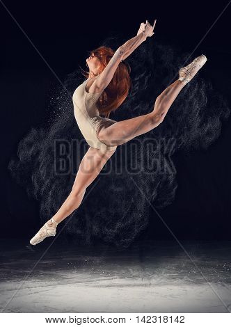 Dancer high jump and the explosion of white dust. Dramatic portrait of strong woman dancer with white powder on black background.