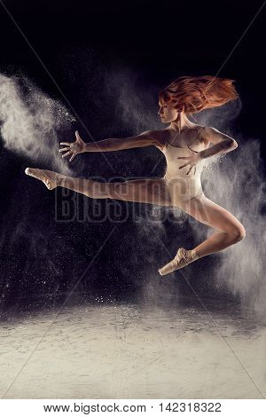 Dancer high jump and the explosion of white dust. Dramatic portrait of strong woman dancer with white powder on black background.