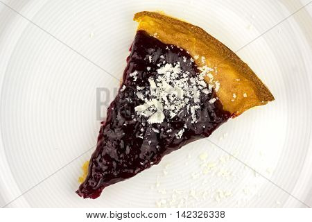 Top down close up view on triangular wedge of tasty red peach cheesecake with white chocolate garnish on white plate