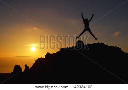 Young woman jumping at a sunset on a mountain of joy on holiday in the air