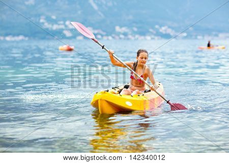 Girl enjoying paddling in kayak on the sea water during summer vacation
