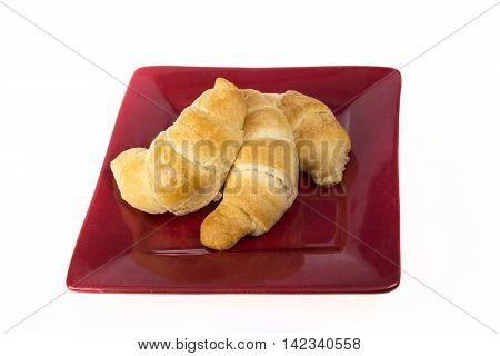 Three fresh flakey buttery croissants on a red plate and isolated on white.