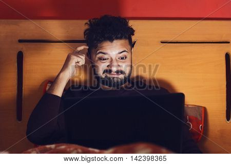 Young man looking at laptop and thinking in dark room browsing on internet