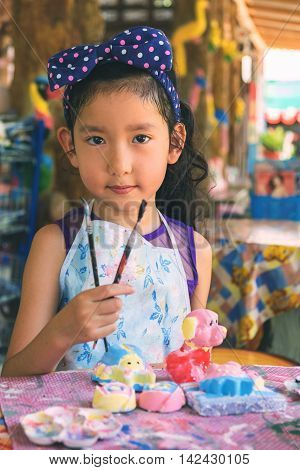 Cute asian girl show her paint brush for painting plaster statue filterd color.