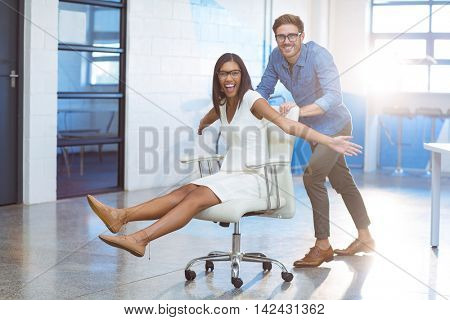 Business executive pushing businesswoman in office chair at workplace