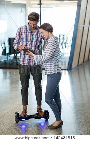 Man on hoverboard using digital tablet with colleagues in office