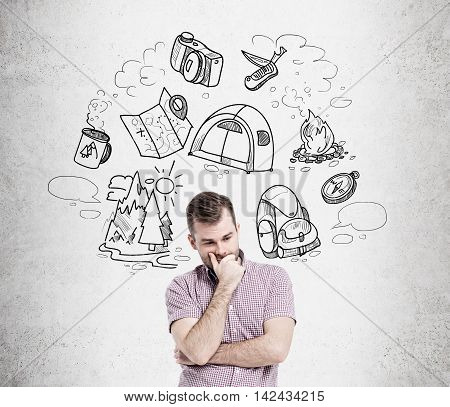 Man in casual clothes thinking about vacation standing against concrete wall with sketches. Concept of rest and relaxation importance.