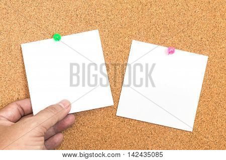 Blank white paper note with green pin on corkboard with hand holding