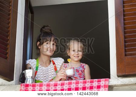Two years old girl with mother are sitting on window sill with traditional European wood brown shutters