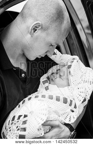 Young father holding his newborn daughter sitting on the back seat of the car.Black and white photography