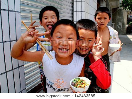 Wan Jia China - June 11 2008: Four young boys using chopsticks to eat their rice and vegetables lunch in front of their school
