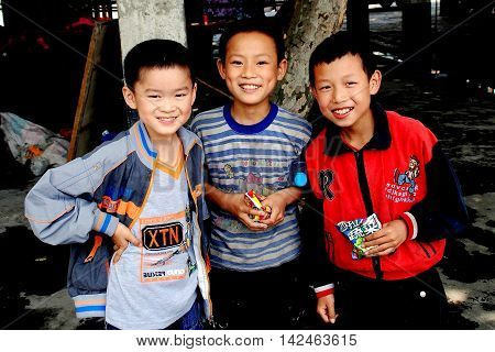 Wan Jia China - June 11 2008 Three smiling schoolboys eating packaged food snacks in the village marketplace