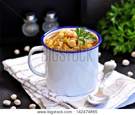 Soup with chickpeas, lentils, rice, beef in a bowl on a black background.