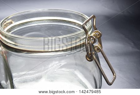 Empty glass jar with the open cap hold with metal wire over the black background