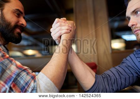 people, leisure, challenge, competition and rivalry concept - close up of male friends arm wrestling at bar or pub