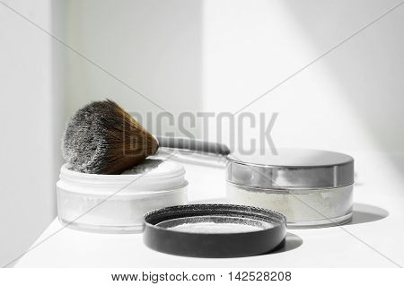 White mineral powder for make-up and big make-up brush on a white table
