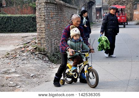 Pengzhou China - December 13 2013: Grandmother teaches her grandson how to ride his bicycle on a rual country road